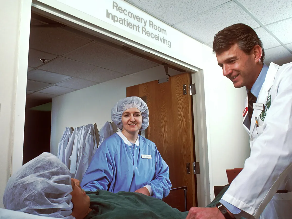 Doctor in a white lab coat with a nurse in blue scrubs beside a patient